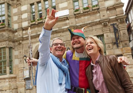 Touristengruppe mit Mann im Rattenfänger-Kostüm nimmt Selfie vor historischem Gebäude in Hameln.