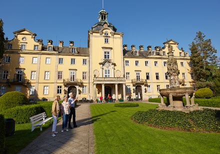 Schloss Bückeburg mit gelber Fassade und Türmchen, umgeben von gepflegten Gärten und Personen.