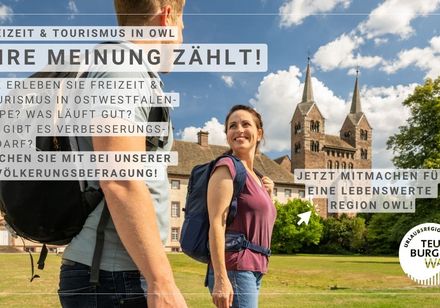 Pärchen mit Rucksack vor dem Westwerk Corvey, mit Text zum Aufruf einer Bevölkerungsumfrage im Teutoburger Wald