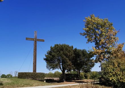 Großes Holzkreuz auf Bergrücken mit Baumbestand an rechter Seite